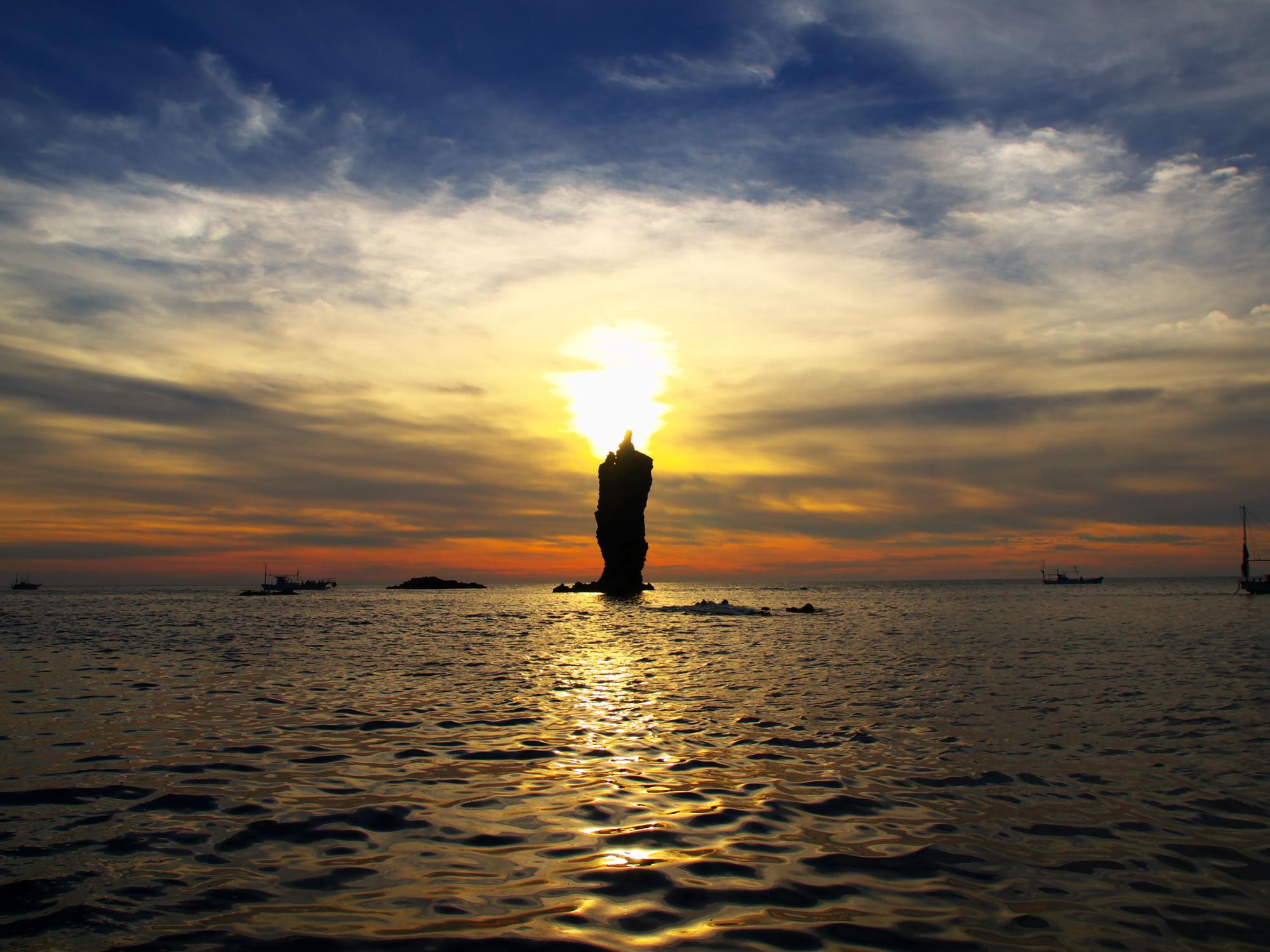 雄大な海と空の間で、太陽の光がローソク島の背後から差す夕暮れの写真