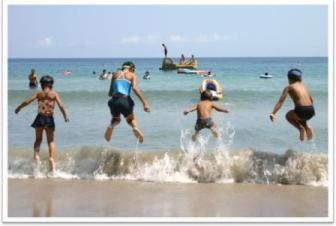 夏の海水浴場で飛び跳ね、水しぶきを上げながら遊んでいる子どもたちの写真