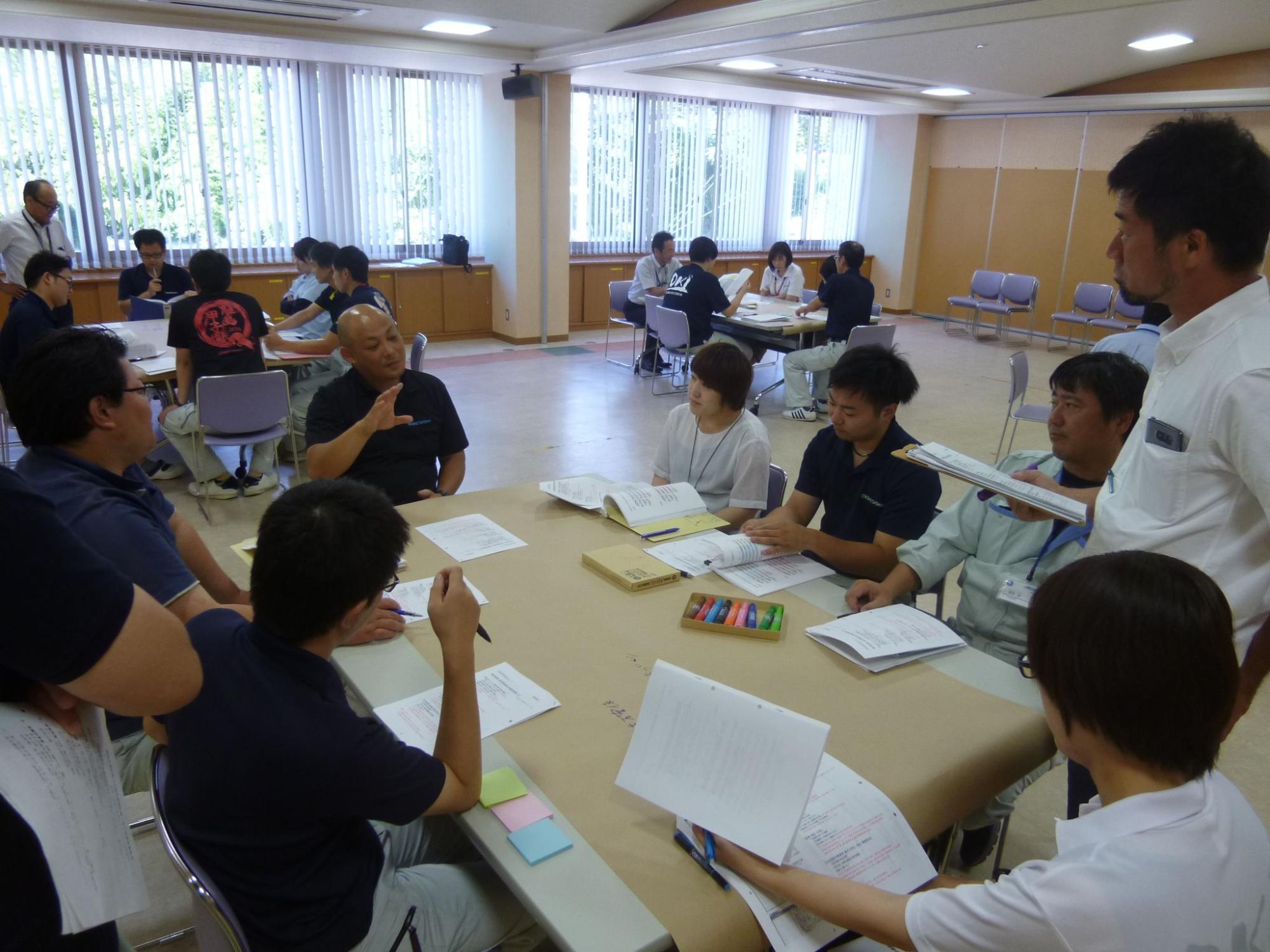 資料を持ちながら話している男性とそれを聞いている職員たちの写真