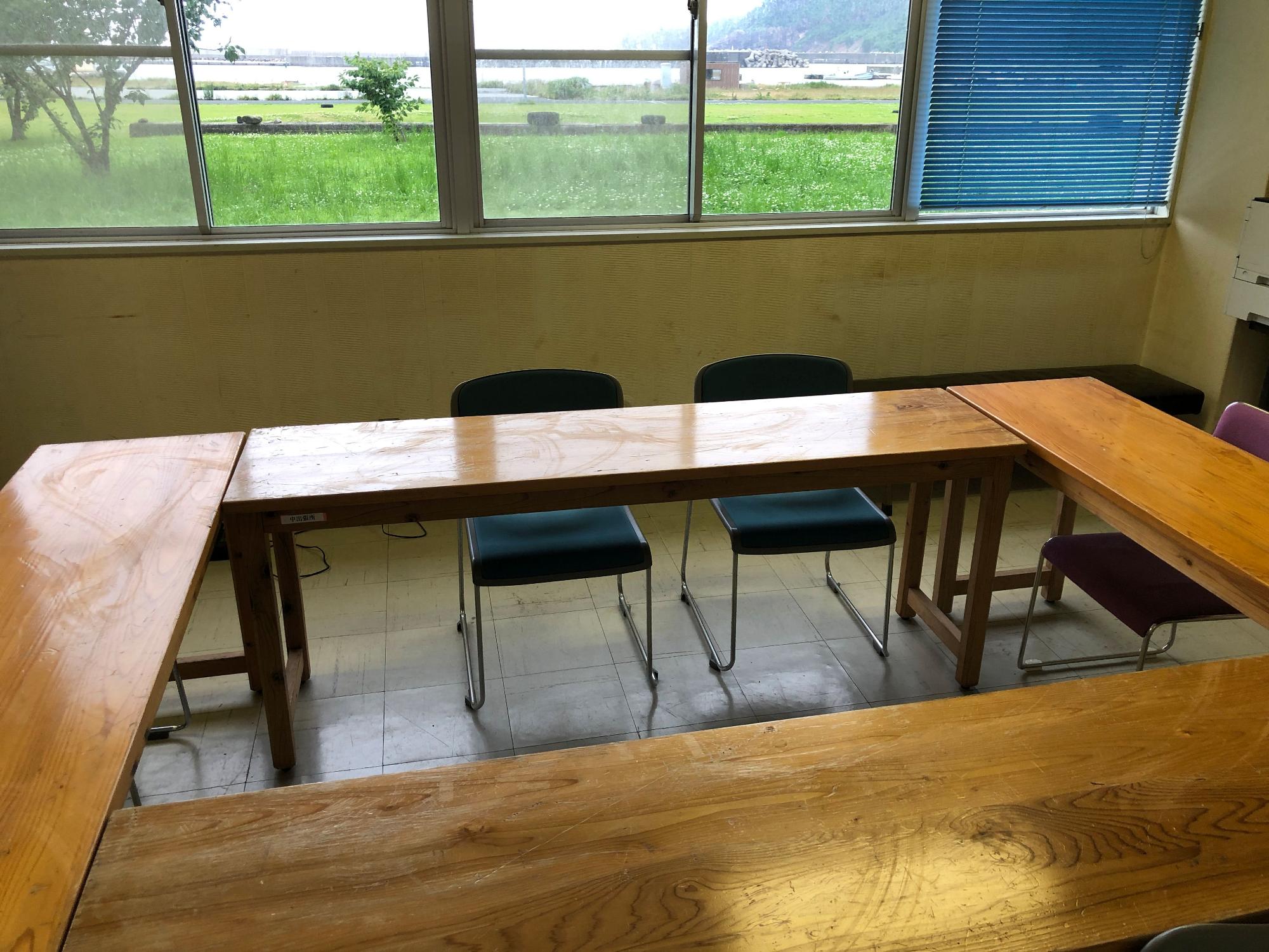 フローリングの部屋に四角く机と椅子が並べられた集会室の写真