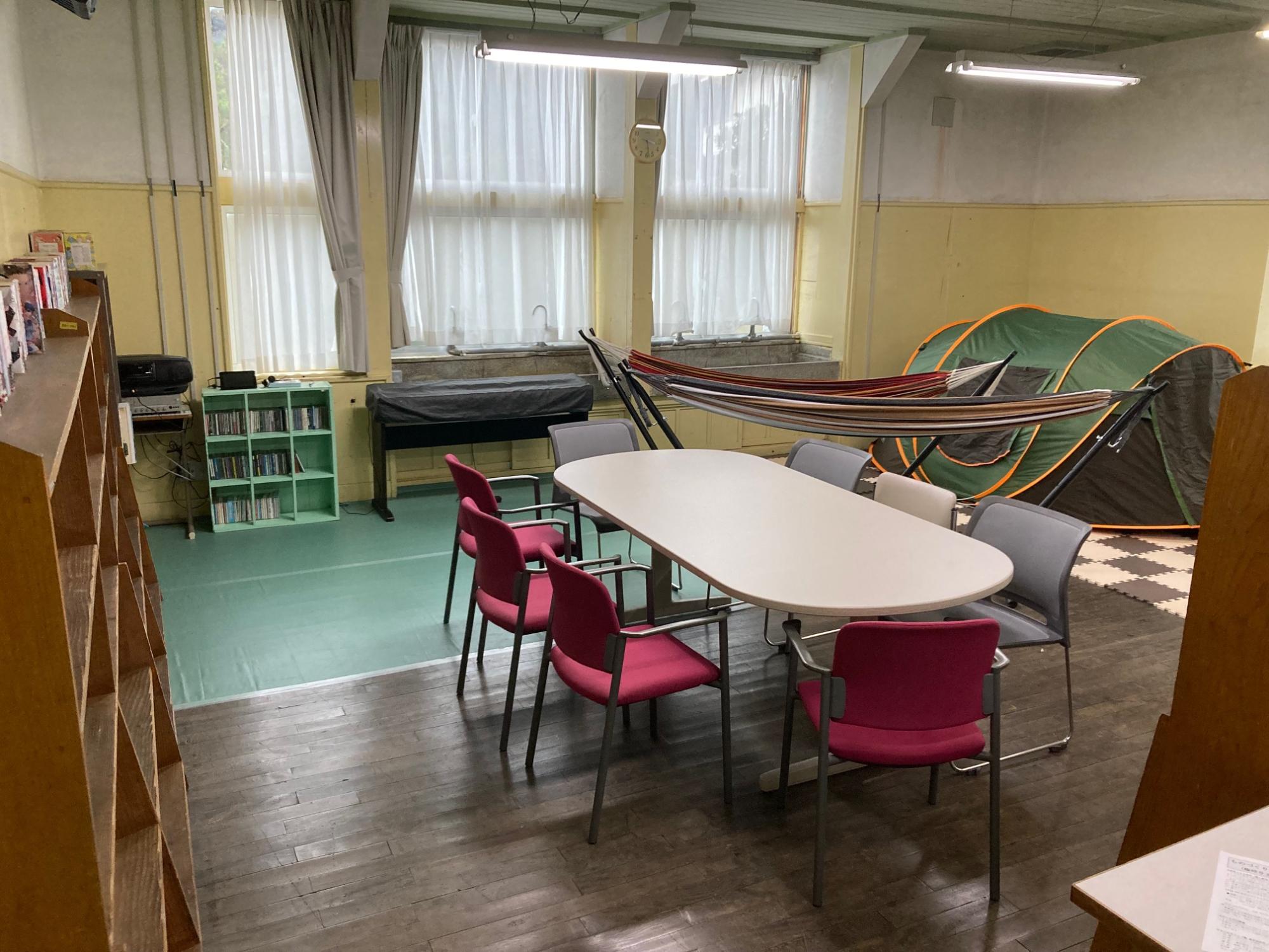 部屋の真ん中に机と椅子、外周にキャンプ用品などが並べられた107号室の写真