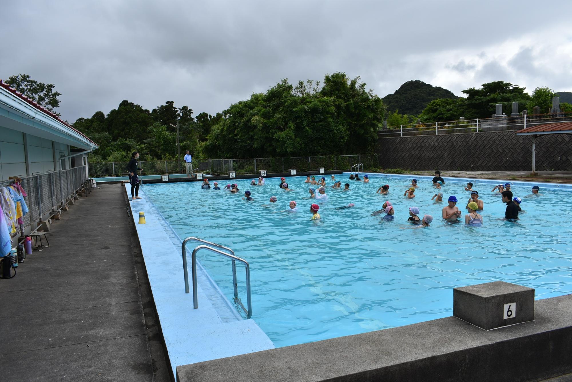 学校の屋外プールで児童たちが水泳の授業をしている写真