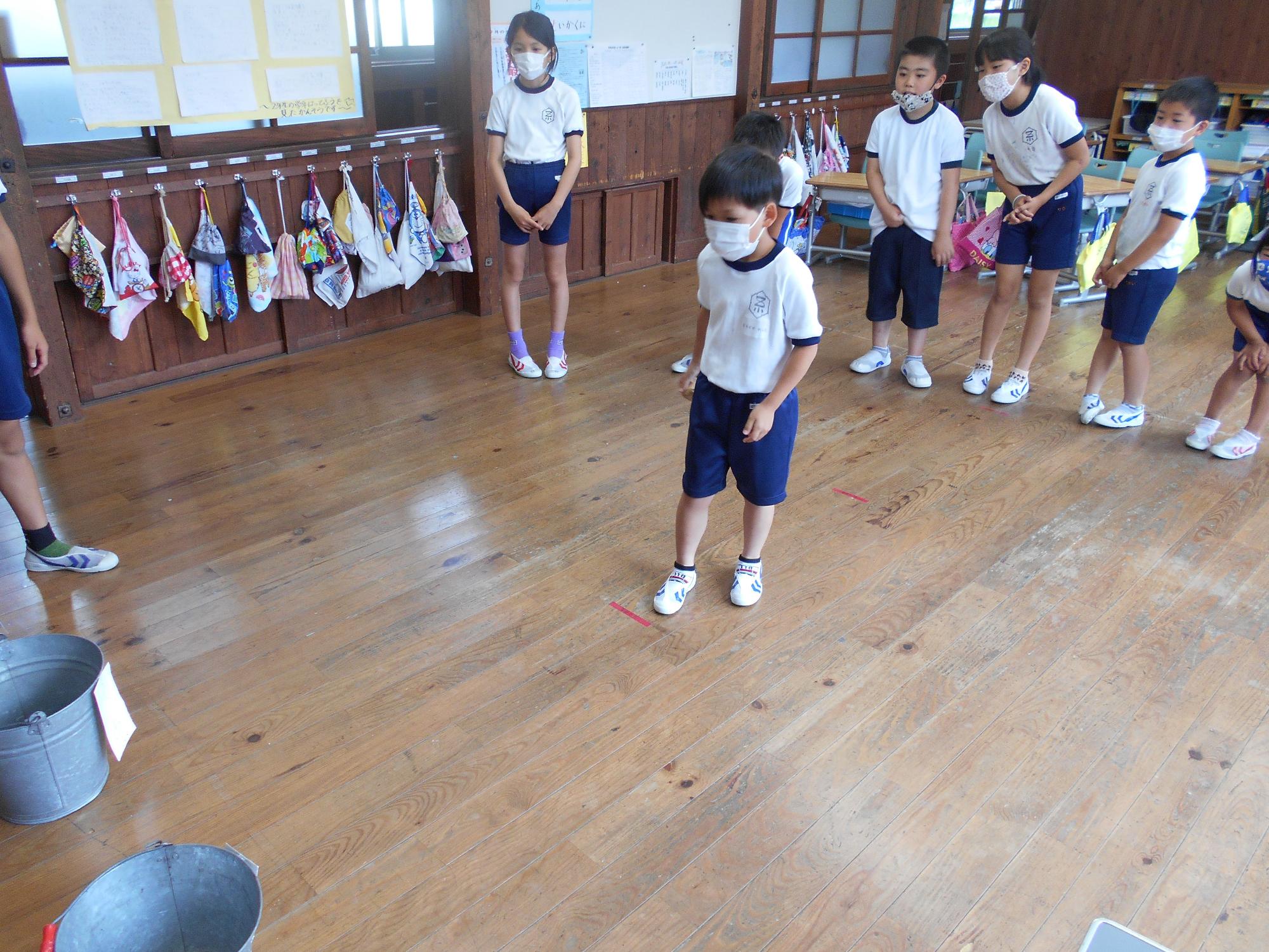 一人の体操着姿の児童が、教室の床に示された赤い線の前に立ってゲームを楽しんでいる様子の写真