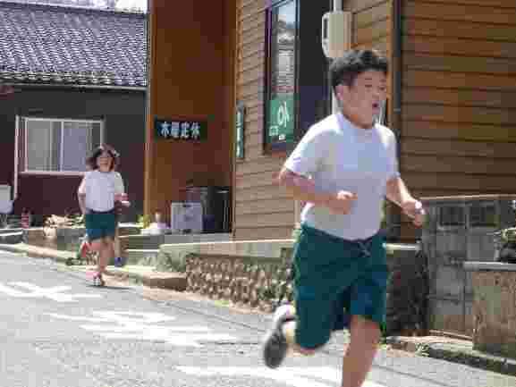 町の通りを走る体操着を着た子どもたちの写真
