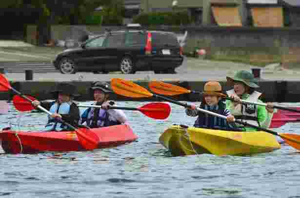 海で色とりどりのカヤックに乗りオールで漕いでいる子どもたちの写真