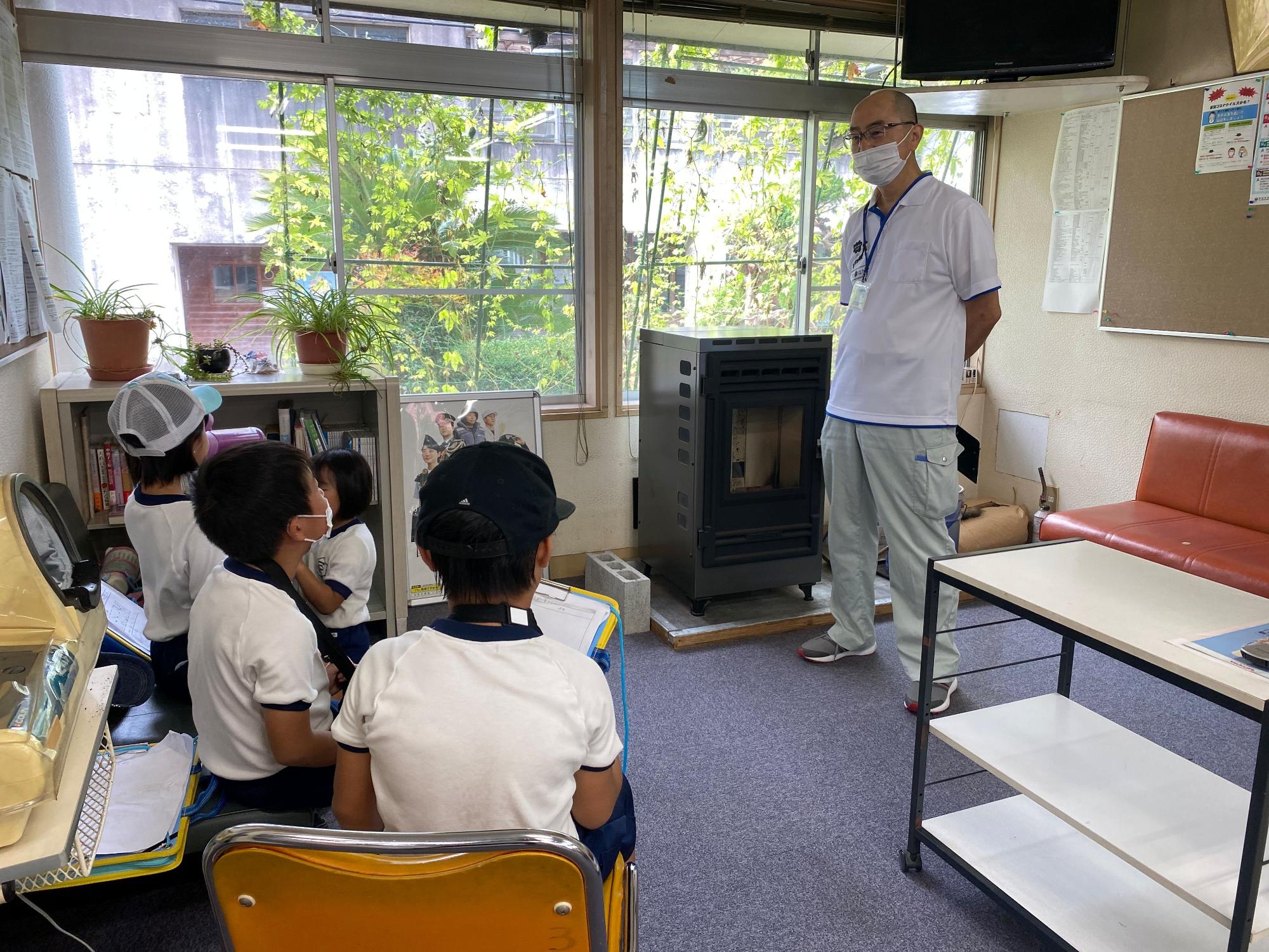 マスクを付けた職員の男性の話を座って聞いている児童たちの写真