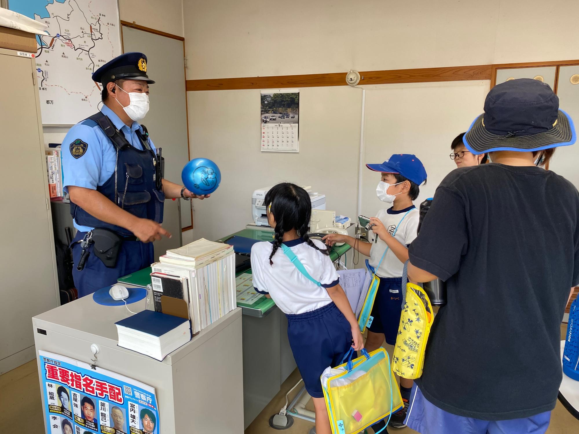 水色のボールを左手に持って説明している警察官の話を聞いている2人の児童の写真