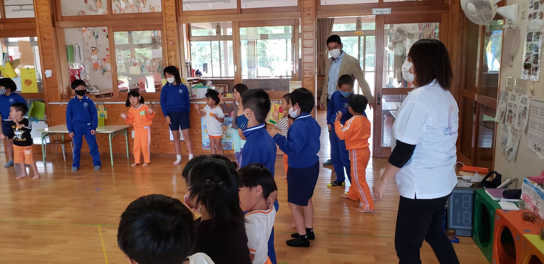 幼稚園の教室で児童と園児が並んで立ち、交流している様子の写真