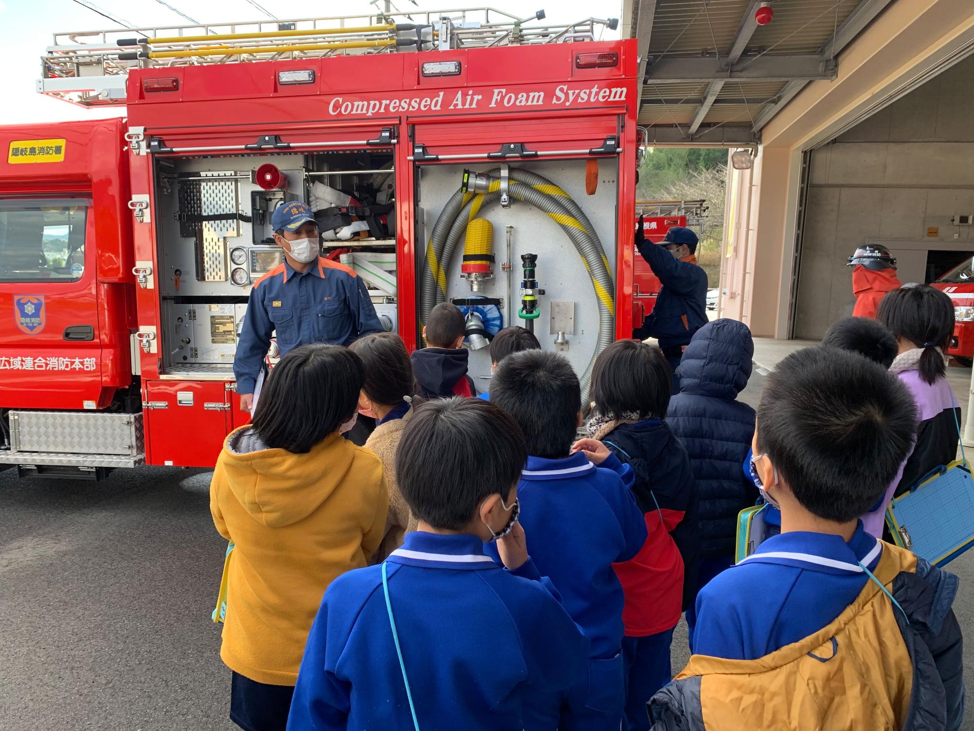 消防車の脇で消防士の方の説明を熱心に聞く児童たちの写真