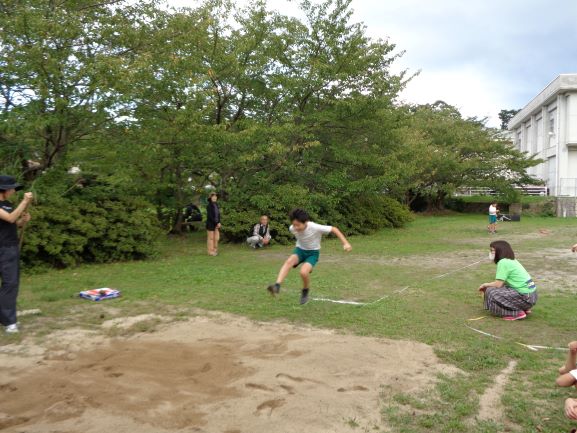 校内に設置された砂場で走り幅跳びを飛んでいる生徒の写真