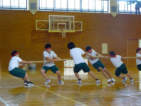 体育館で赤いハチマキをつけた生徒たちが一生懸命綱引きをしている写真