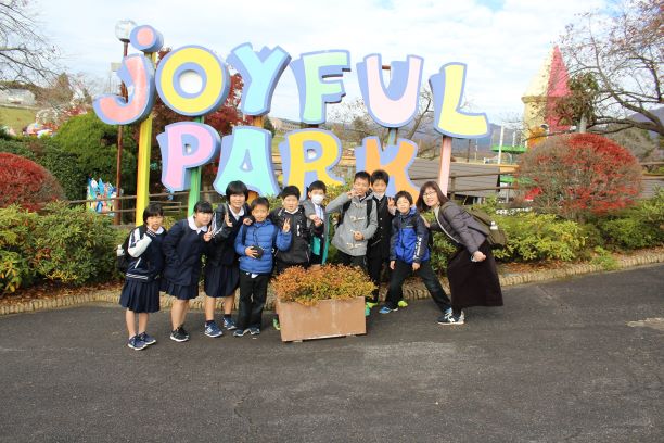 ジョイフルパークと英語で書かれた看板の前で笑顔でピースサインを作っている生徒たちの写真