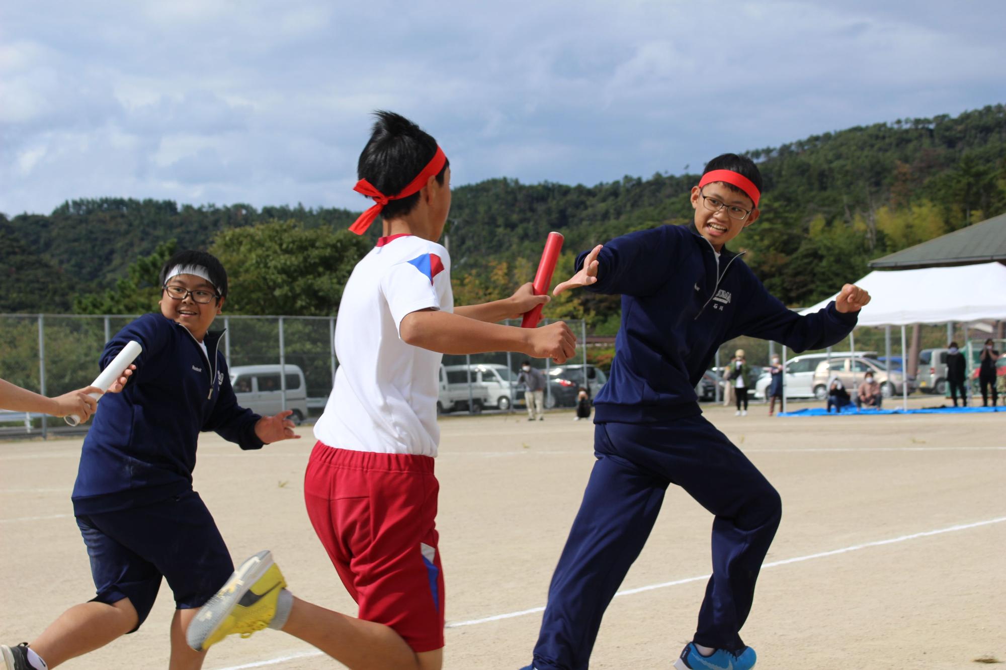 グラウンドでリレーのバトンをつなぐ生徒たちの写真