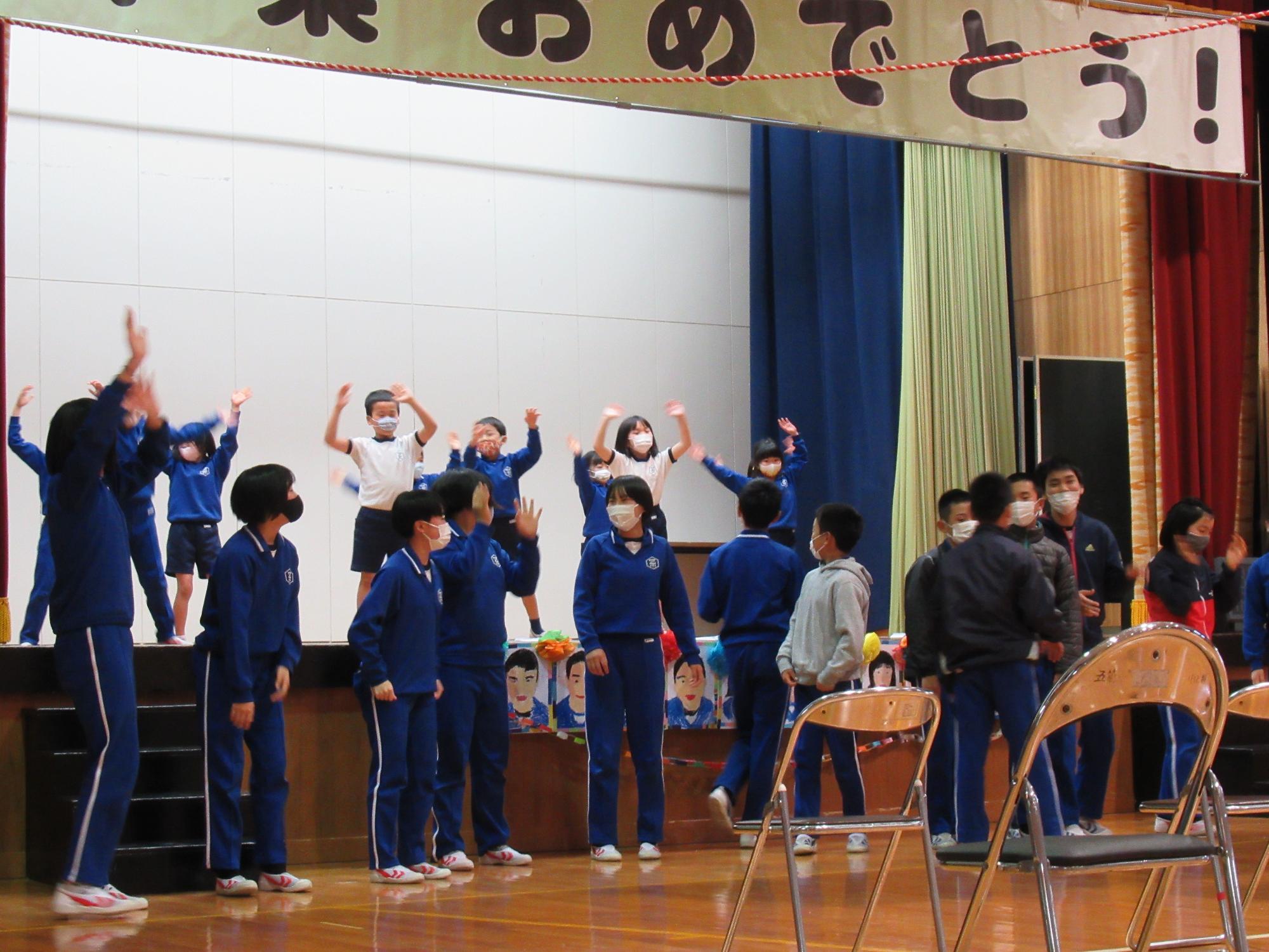 体育館でジャージを着た児童たちが練習を行っている写真