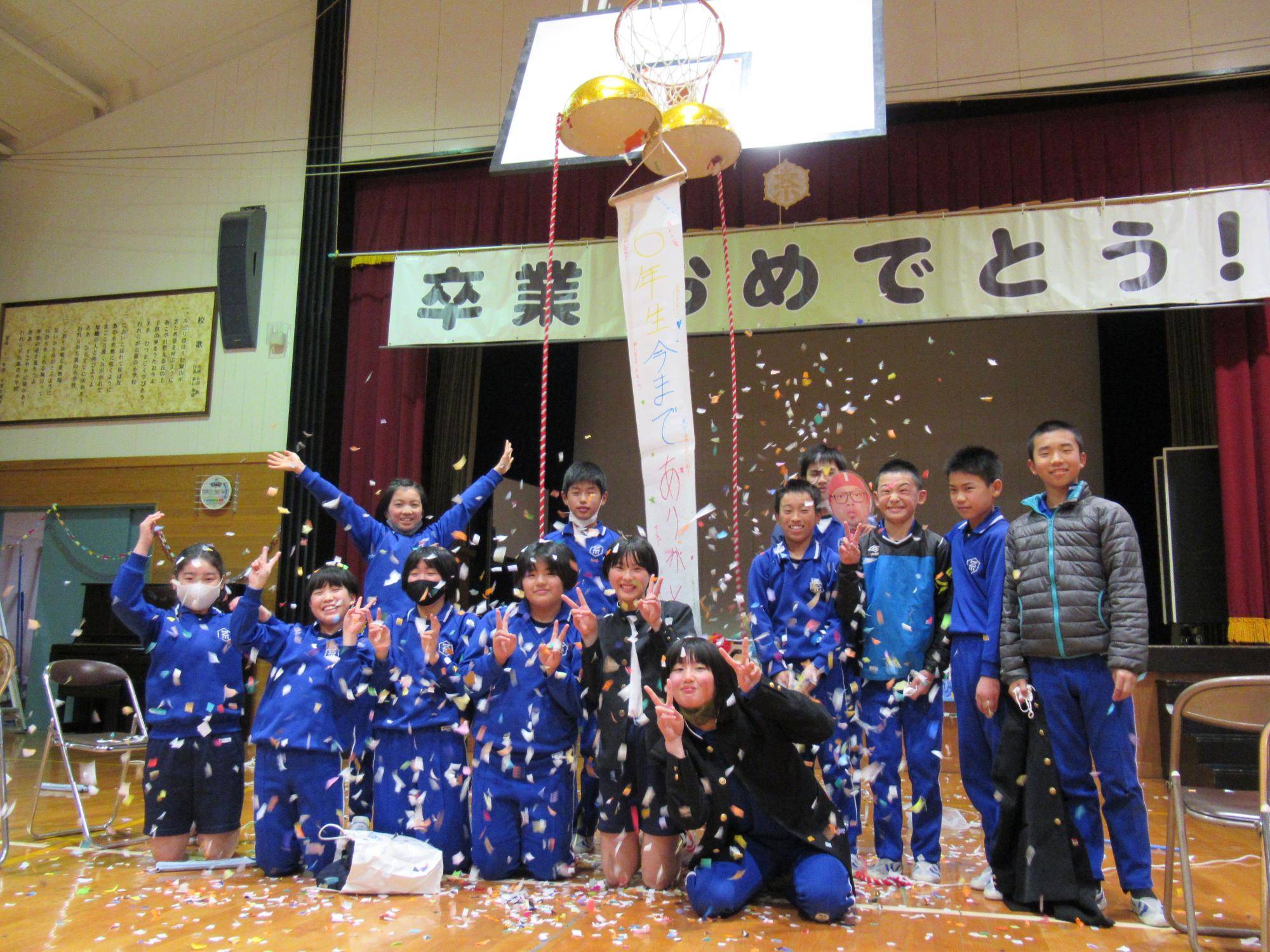 体育館で児童たちがくす玉を割り、記念撮影を行っている写真