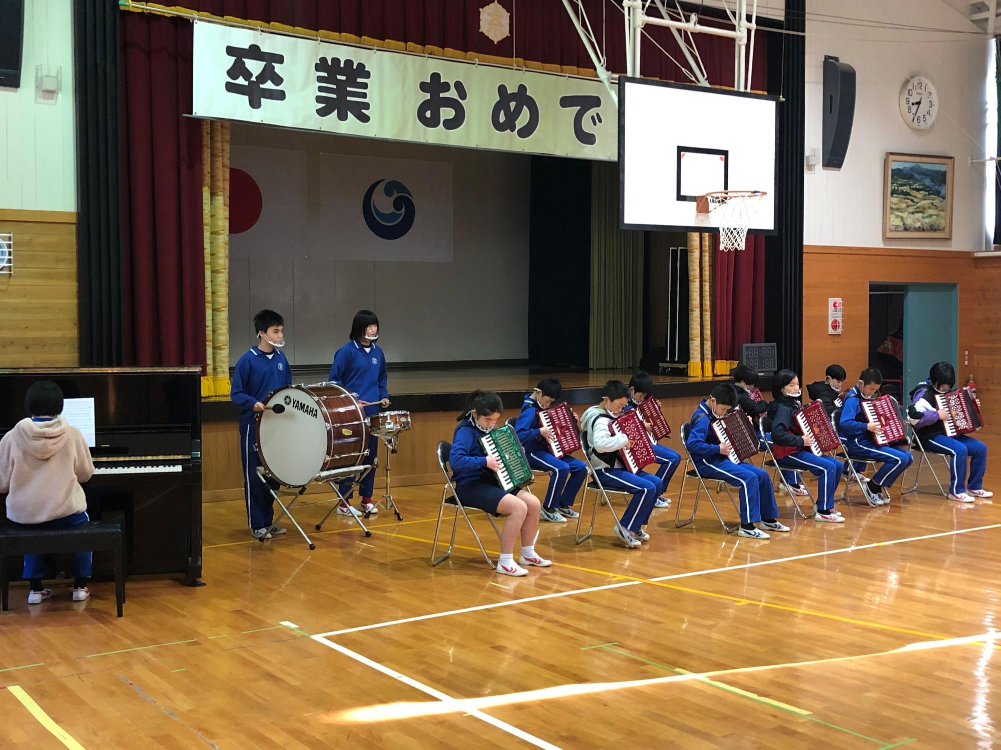 体育館で児童たちが楽器を用いて演奏している写真