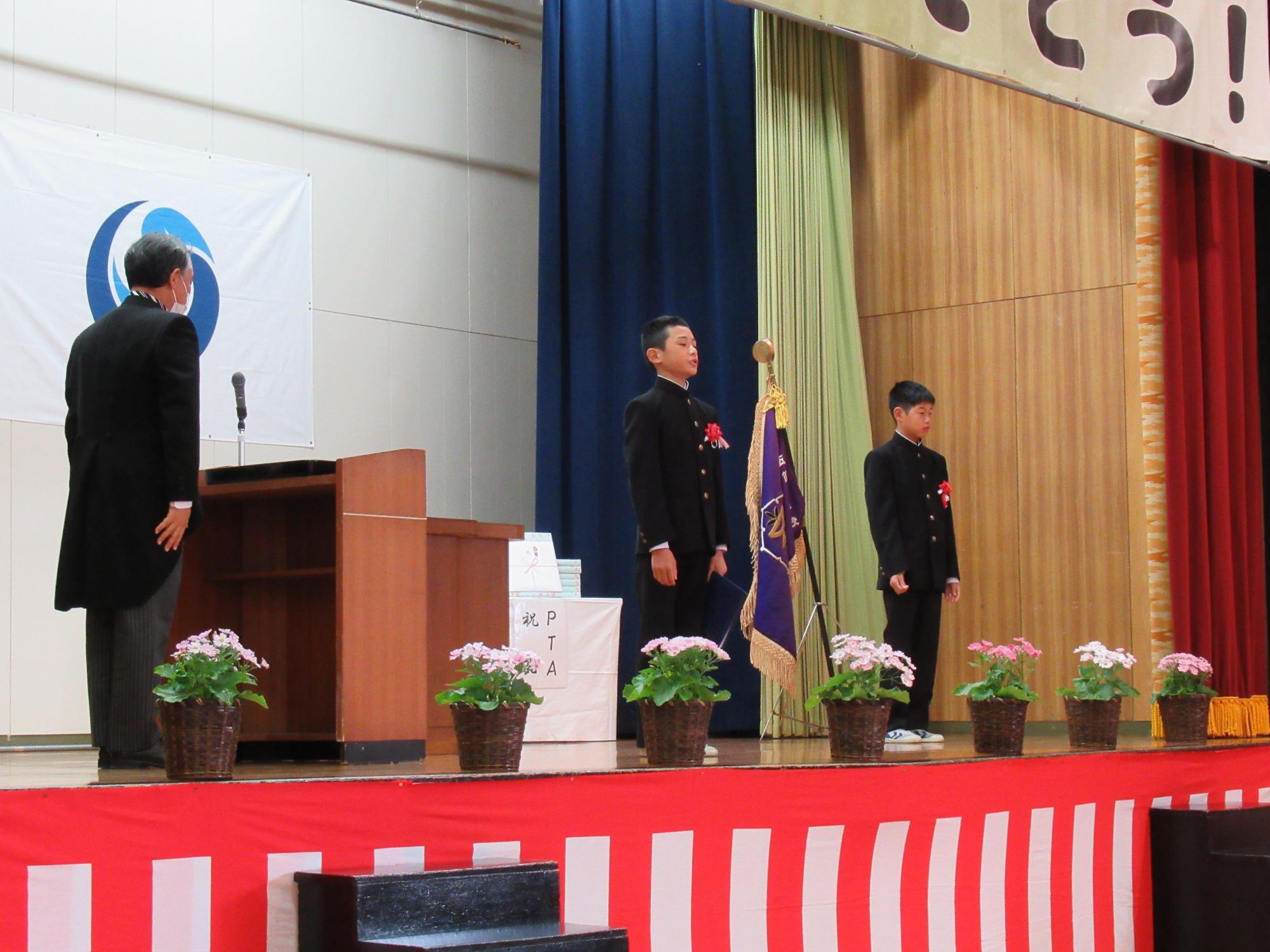 卒業証書授与式でステージの上に立つ児童2人が起立して正面を向いている写真