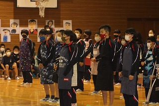 体育館でエプロン姿の児童たちが整列して発表をしている写真