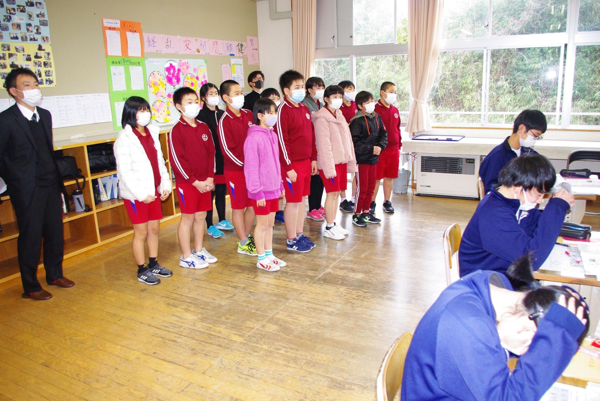 教室で児童たちが先生と一緒に上級生の授業を見学している写真