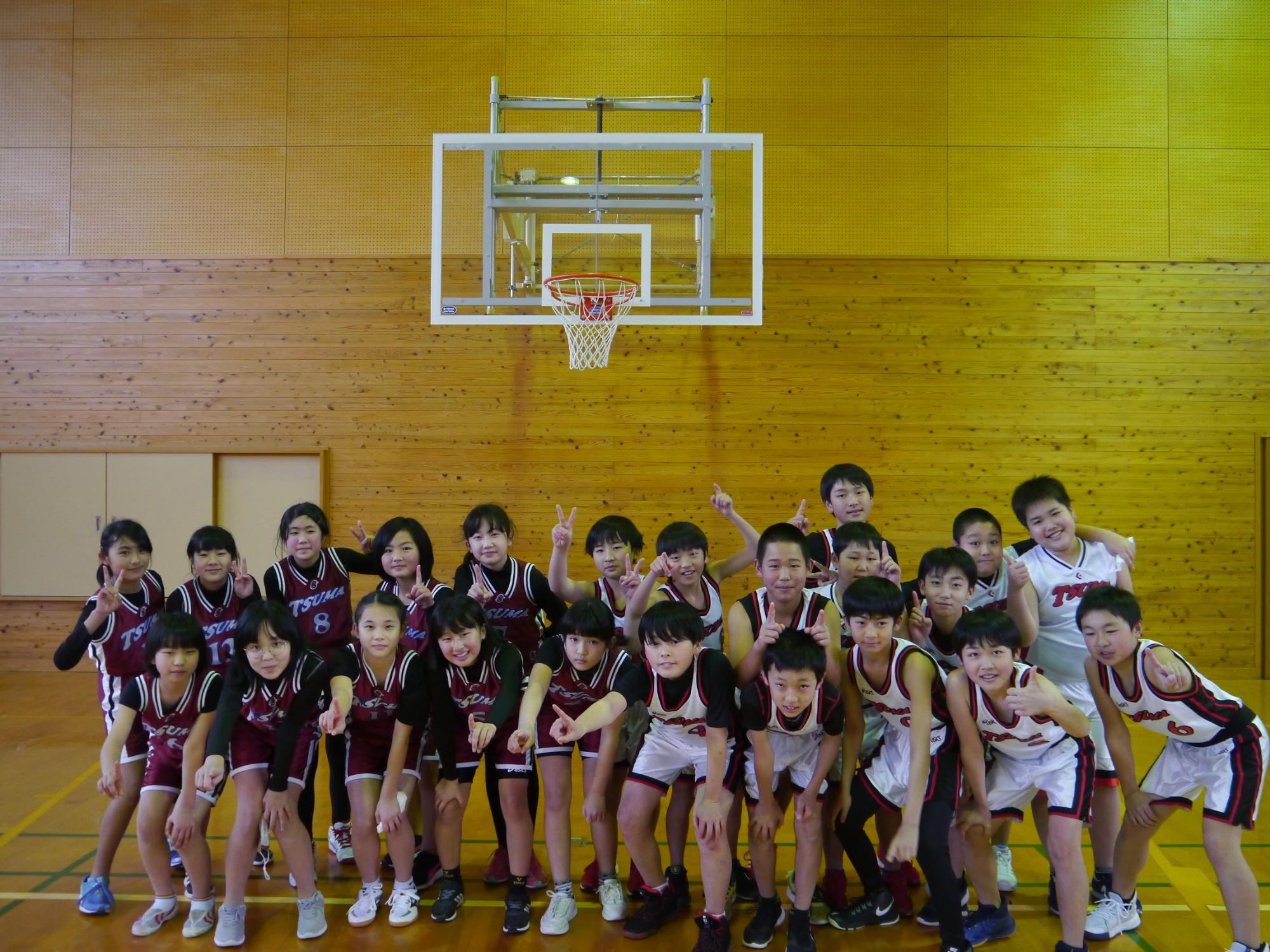 体育館のバスケットゴール前で男女の児童たちが集合写真を撮っている写真
