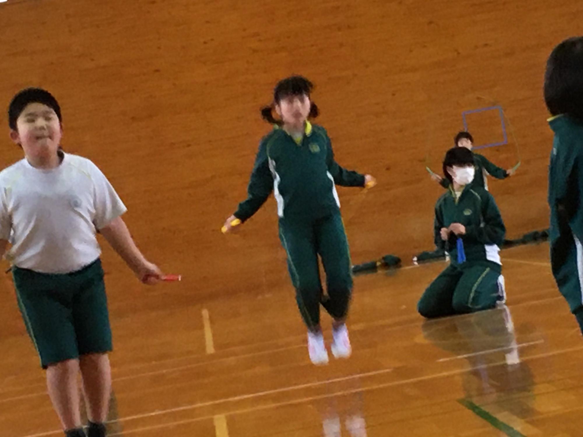 体育館で2人の男女の児童が縄跳びを飛んでいる写真