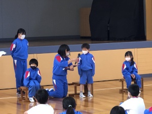 体育館で高学年の児童が低学年の児童に対してインタビューを行っている様子の写真