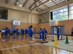 体育館で児童たちが木製の高跳び台の調整を行っている様子の写真