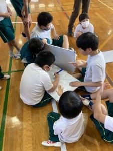 体育館で児童たちがホワイトボードを囲んで話し合っている写真