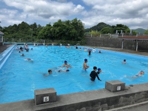 学校のプールで気持ちよさそうに泳ぐ子どもたちの写真