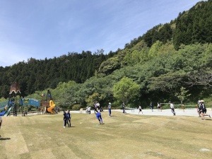 公園の芝生広場で児童たちが元気に遊んでいる写真