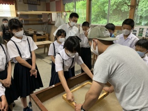 紙すき体験で児童が指導を受けながら紙を作っている写真
