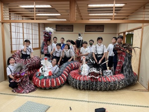 和室で児童たちが大蛇の模型と一緒に集合写真を撮っている写真