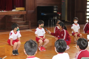 体育館で児童が司会のインタビューに答えている写真