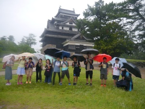 松江城の前で児童たちが傘を差して集合写真を撮っている写真