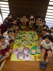 体育館で児童たちが黄組のポスターを囲んで記念撮影している写真