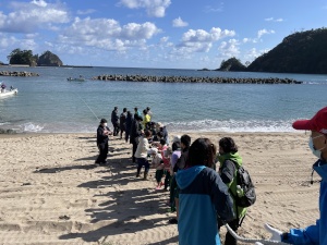 海岸で児童と地域の人々が綱を引いている写真