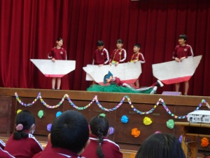 体育館の舞台で児童が劇を発表する写真