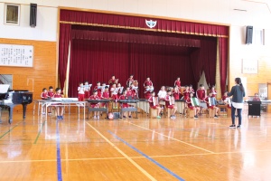 体育館の舞台で児童が合奏を披露する写真