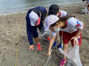 海辺で児童がごみ拾いをする写真