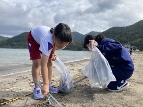 浜辺で児童がごみを袋に集める写真