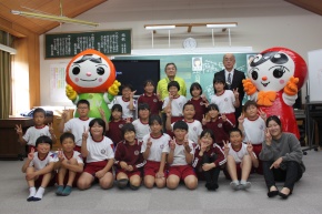 教室でキャラクターと児童と先生が集合写真を撮る写真