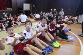 体育館で児童が給食を食べる写真