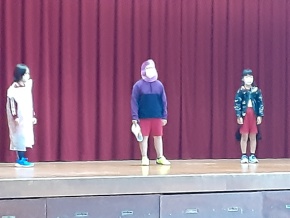 体育館の舞台で児童が劇を発表する写真