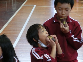 体育館で児童が焼きいもを食べる写真