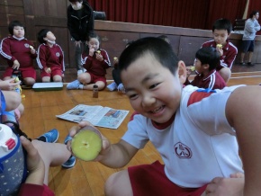体育館で児童が焼きいもを見せる写真