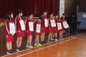 体育館で「6年生ありがとう」の文字を掲げて並ぶ児童たちの写真