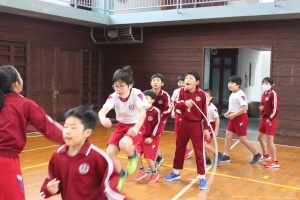 体育館で列になって一斉に大縄跳びをしている児童たちの写真