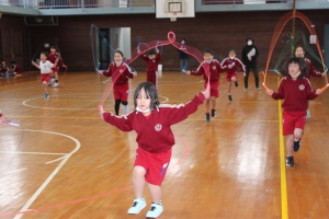 体育館で赤い体操服を着た児童たちが縄跳びをしている写真