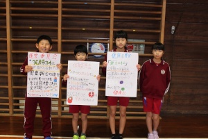 体育館の壁の前で目標ポスターを掲げる児童たちの写真