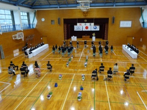 体育館で先生や親御さんたちが見守る中、卒業式が行われている様子の写真